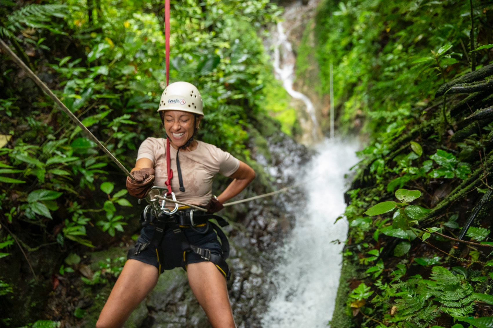 a happy female traveller rappels down a Costa Rican waterfall
