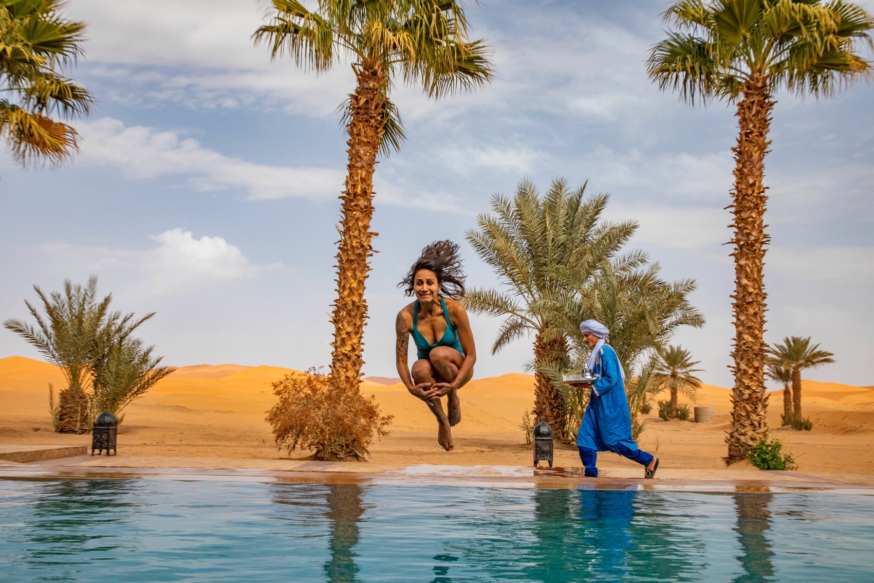 a happy female traveller cannonballs into a desert oasis pool