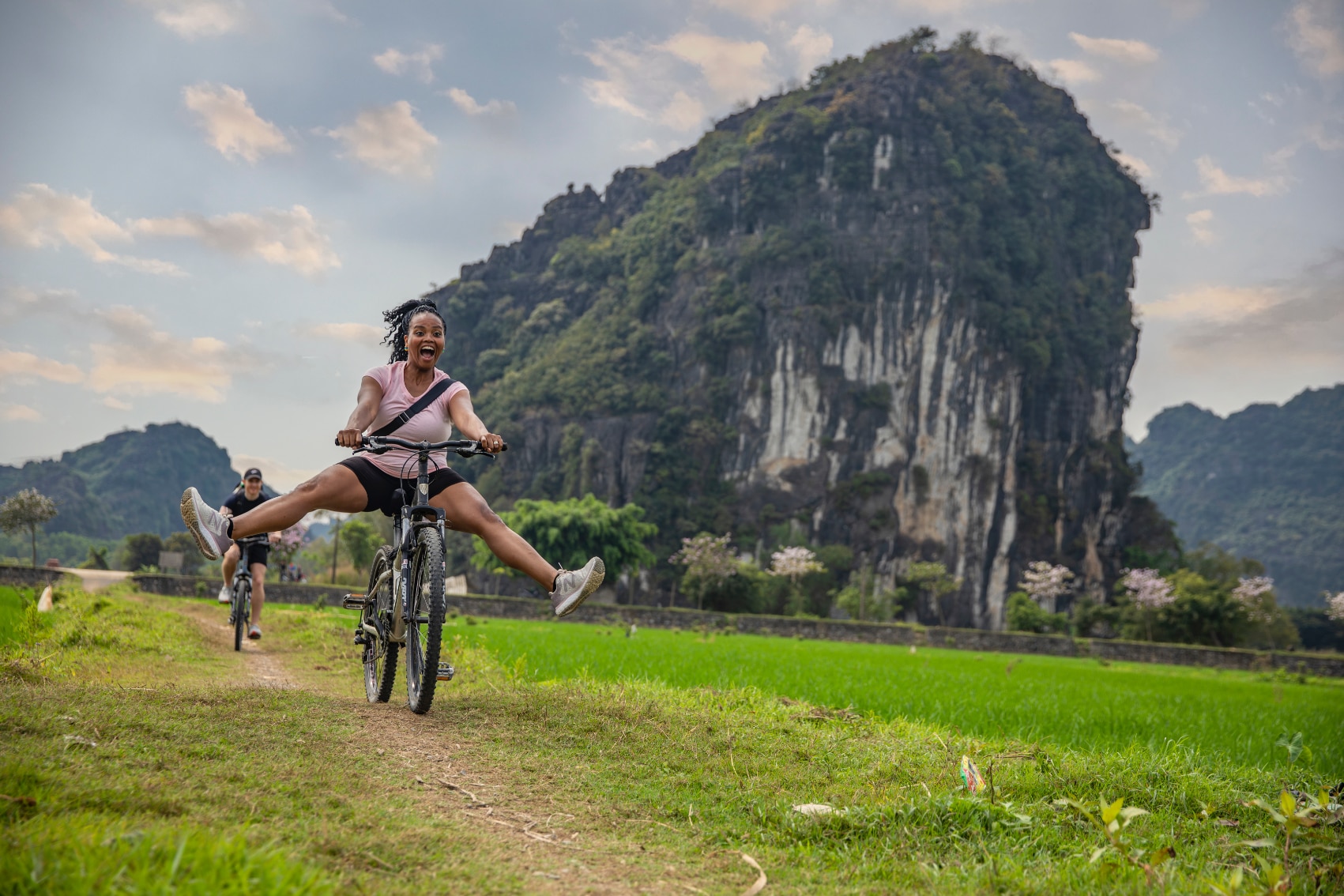 a smiling female traveller bikes past limestone karsts in Vietnam